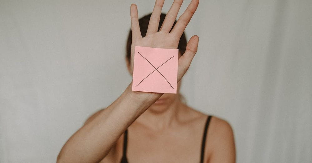 Unrecognizable young woman demonstrating prohibition sign showing gesture of refuse using hand and note with sign stop