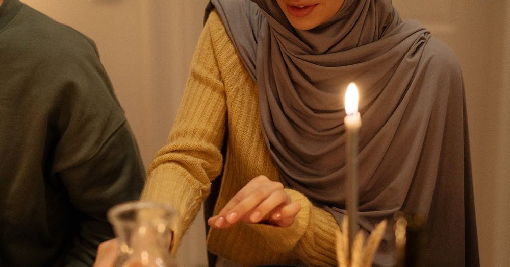 A Woman in Knitted Sweater Wearing Gray Hijab while Sitting Near the Table