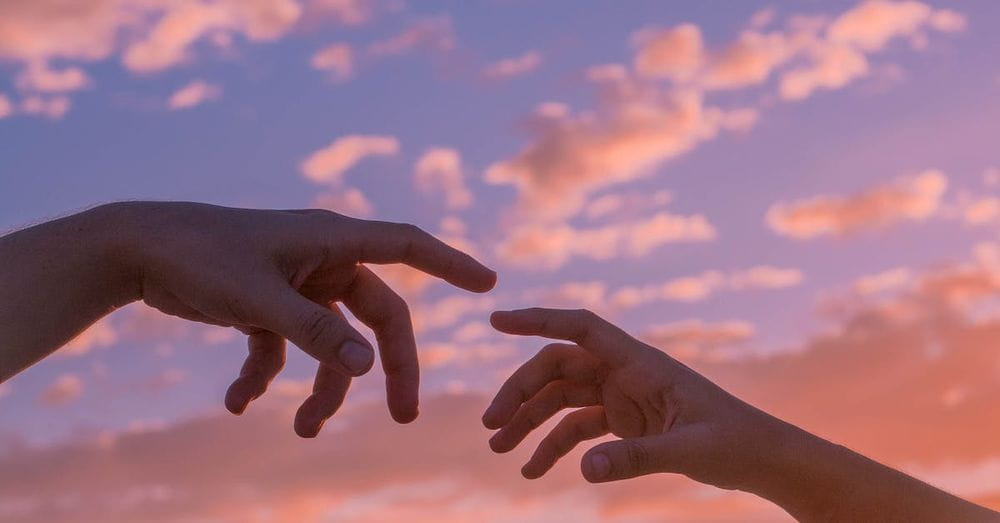 Crop anonymous people pulling hands to each other against bright sunset sky with clouds