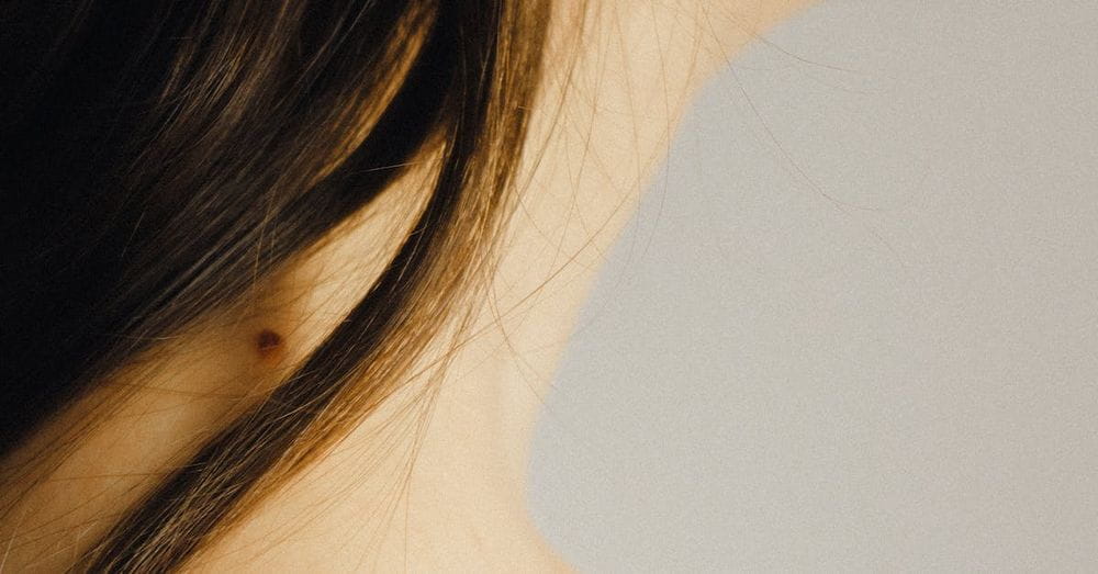 Closeup side view of crop unrecognizable young lady with mole on neck with perfect skin under long dark hair on white background