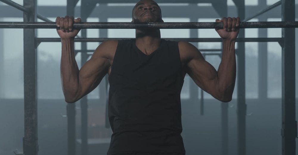 A Man in Black Tank Top Holding on Metal Bars