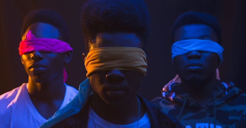 Anonymous cool ethnic male band with Afro hairstyle and covered eyes illuminated by artificial light