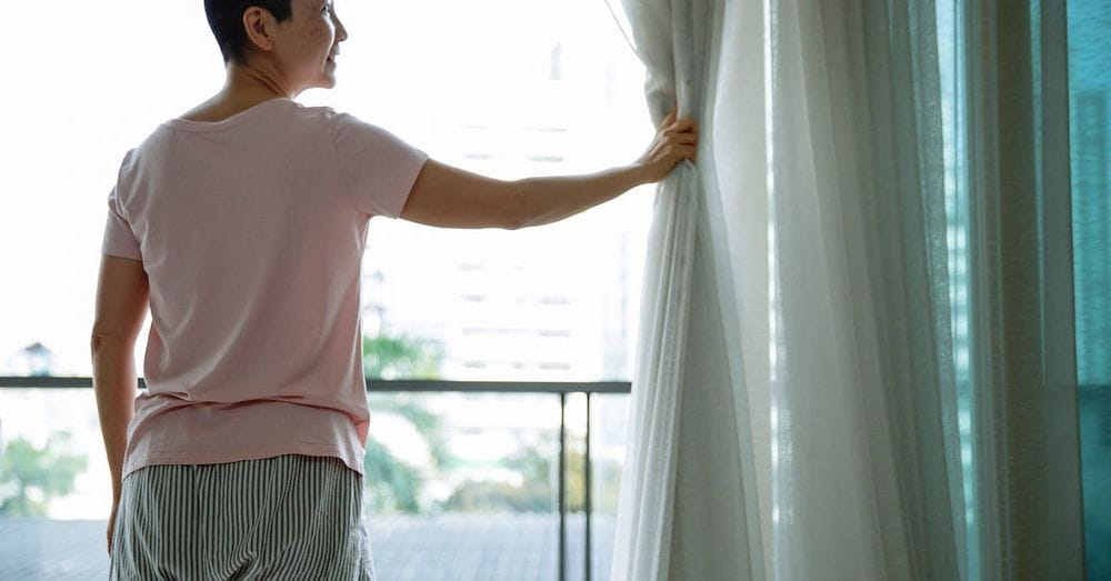 Happy Asian woman with short hair opening curtains of window