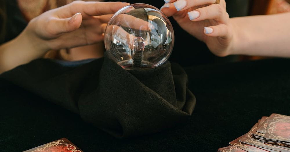 Crop unrecognizable female fortune tellers reading future with magical crystal ball and tarot cards during spiritual session