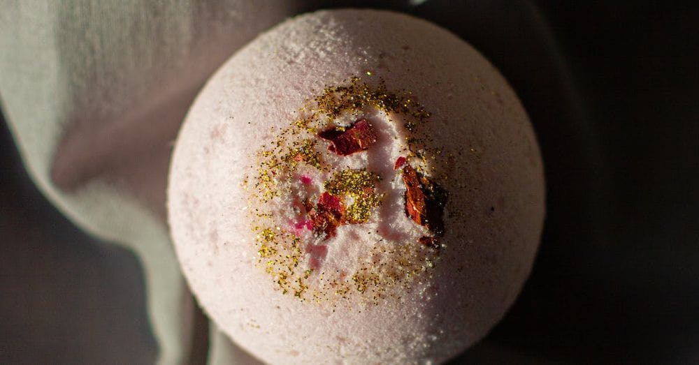 Top view pink fragrant bath bomb in shape of ball placed on dark cloth