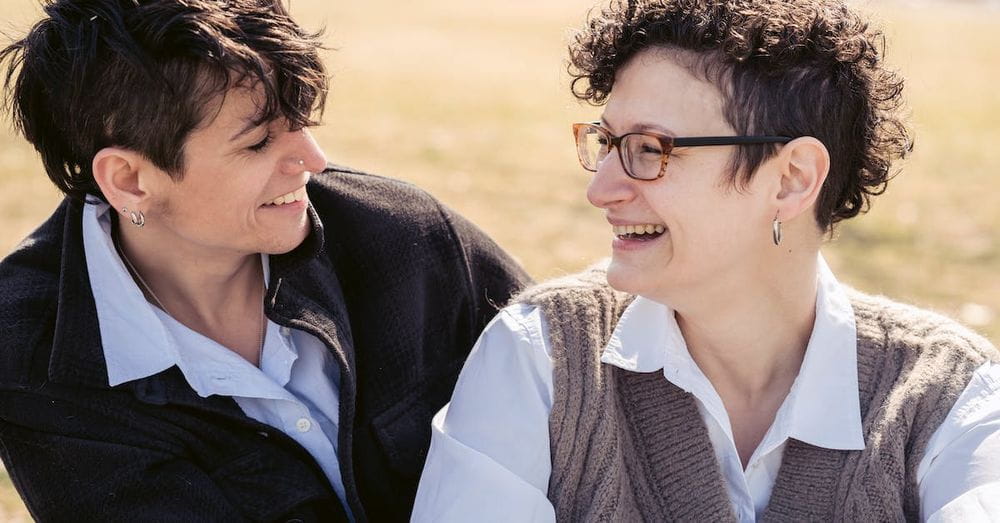 Joyful young lesbian couple laughing and hugging on lawn in park