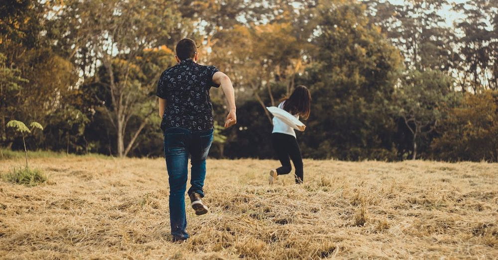 Unrecognizable couple running on meadow in park